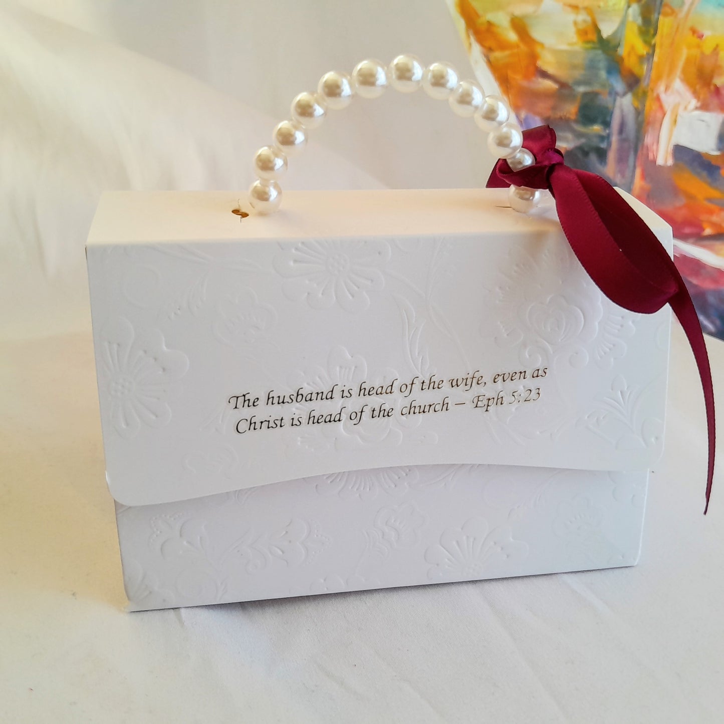 White gift box with pearl handle and red ribbon, featuring a biblical quote.