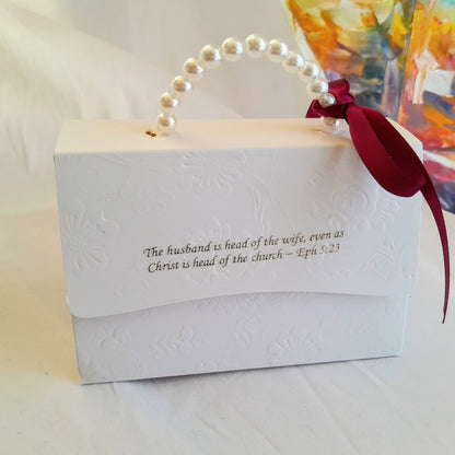 White gift box with pearl handle and red ribbon, featuring a biblical quote.