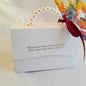 White gift box with pearl handle and red ribbon, featuring a biblical quote.
